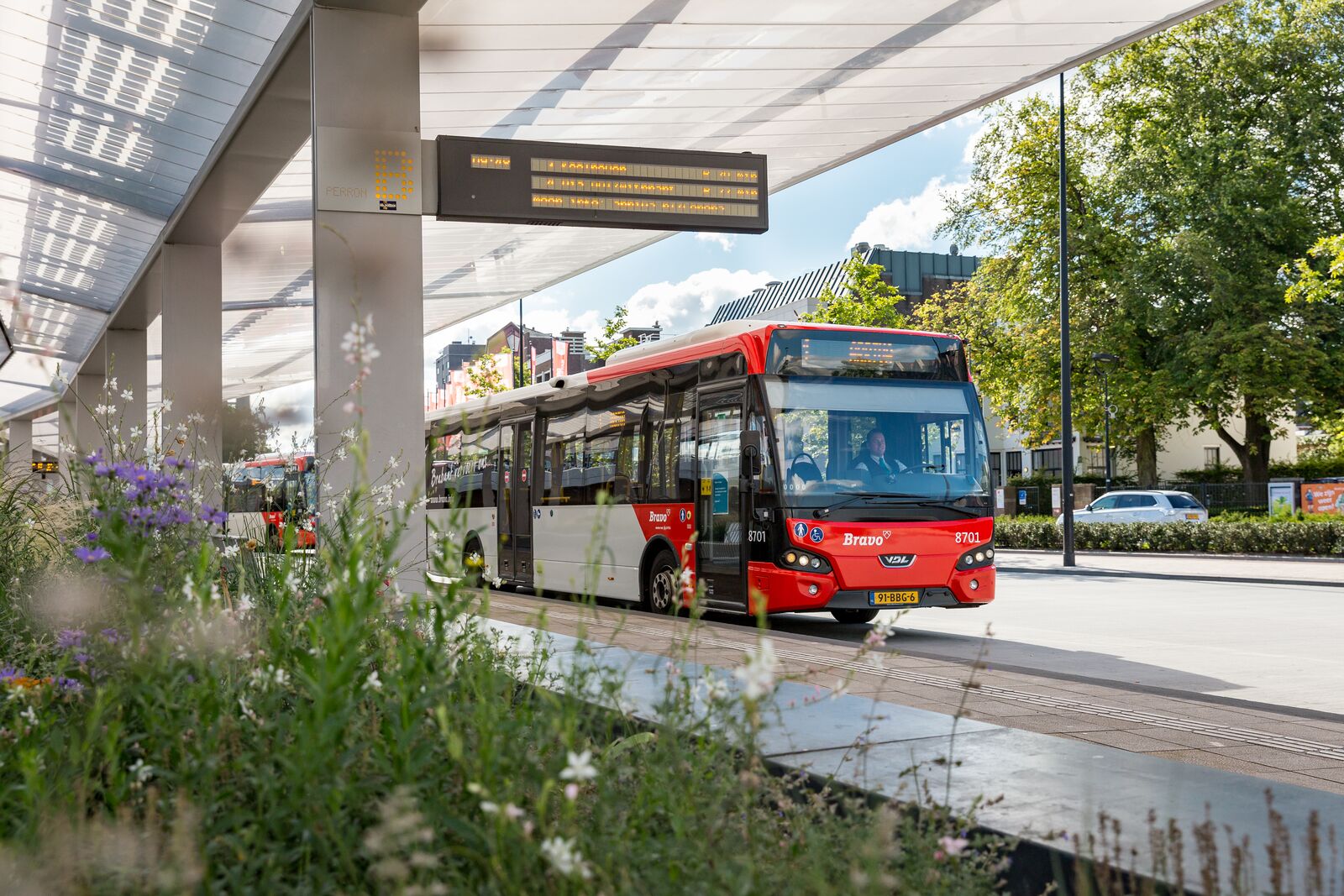 Een rode bus van Arriva staat bij een bushalte onder een overkapping op het voorplein bij treinstation Tilburg.