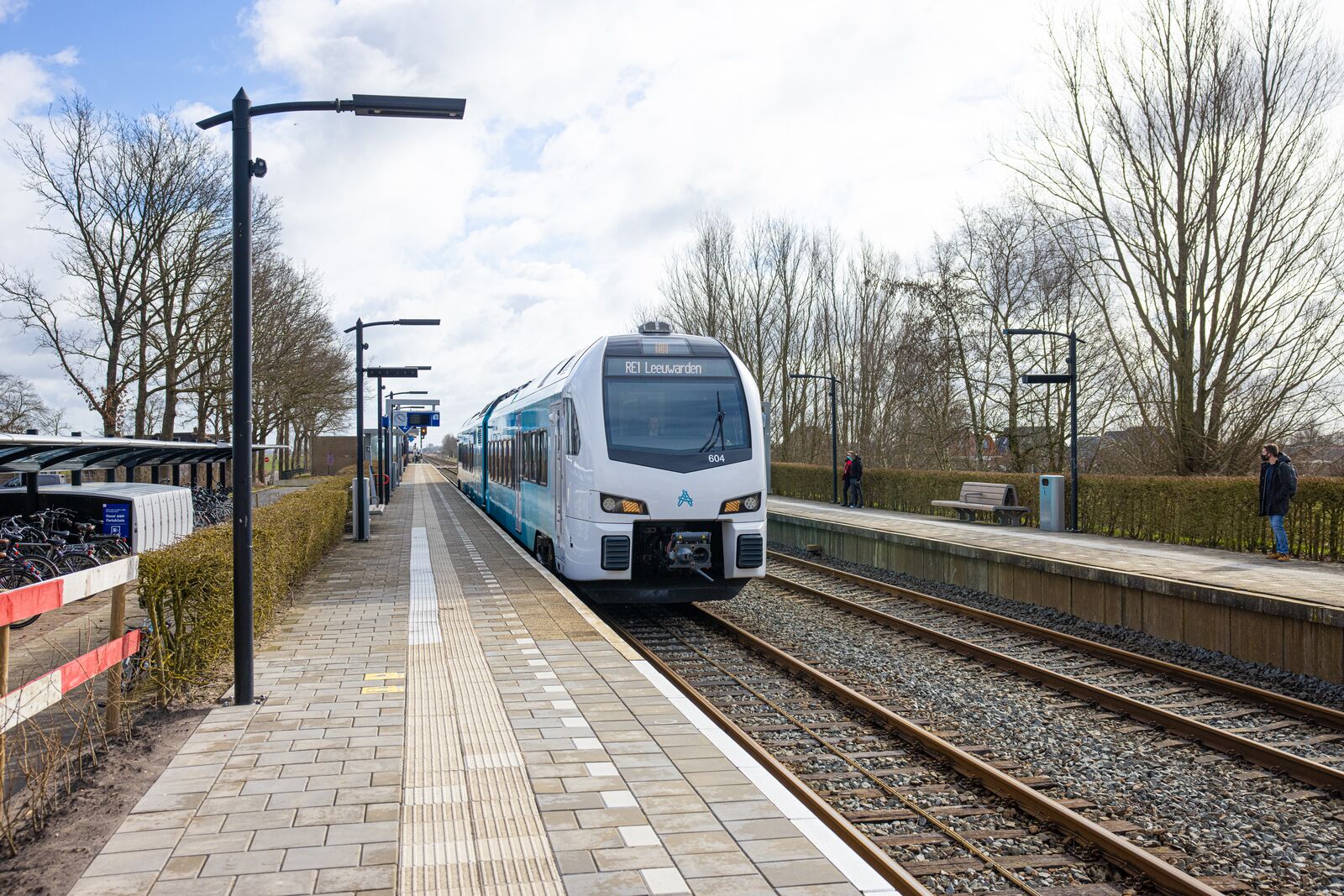 Blauwe trein van Arriva richting Leeuwarden staat stil op een klein station bij een leeg perron op een winterse dag.