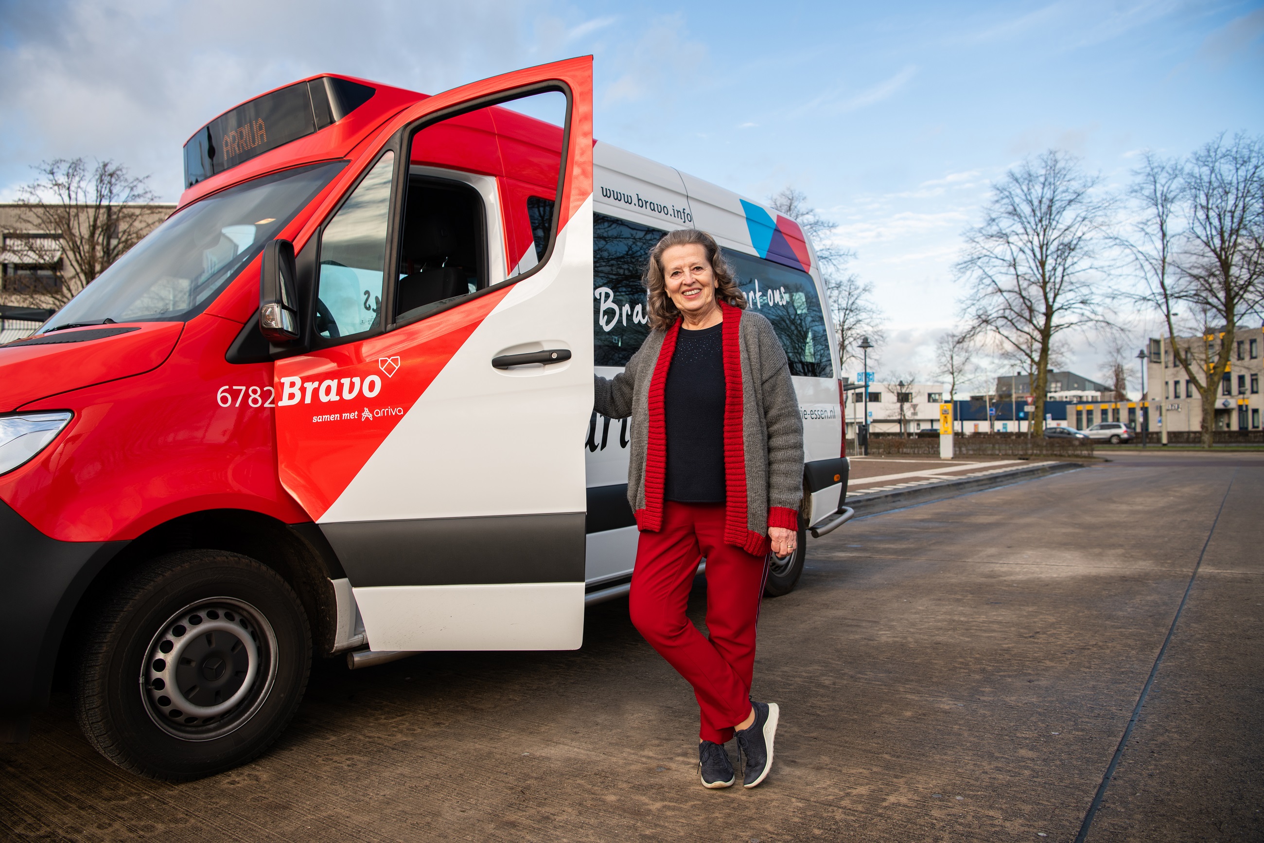 Lachende vrouw staat naast open deur van rood-wit buurtbusje in Brabant.