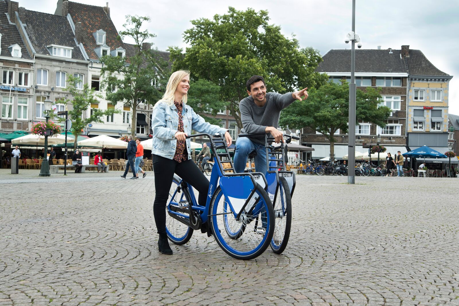 Een man en vrouw staan met hun Arriva deelfiets op een plein in Limburg. Hij wijst en en lacht en zij kijkt in die richting.