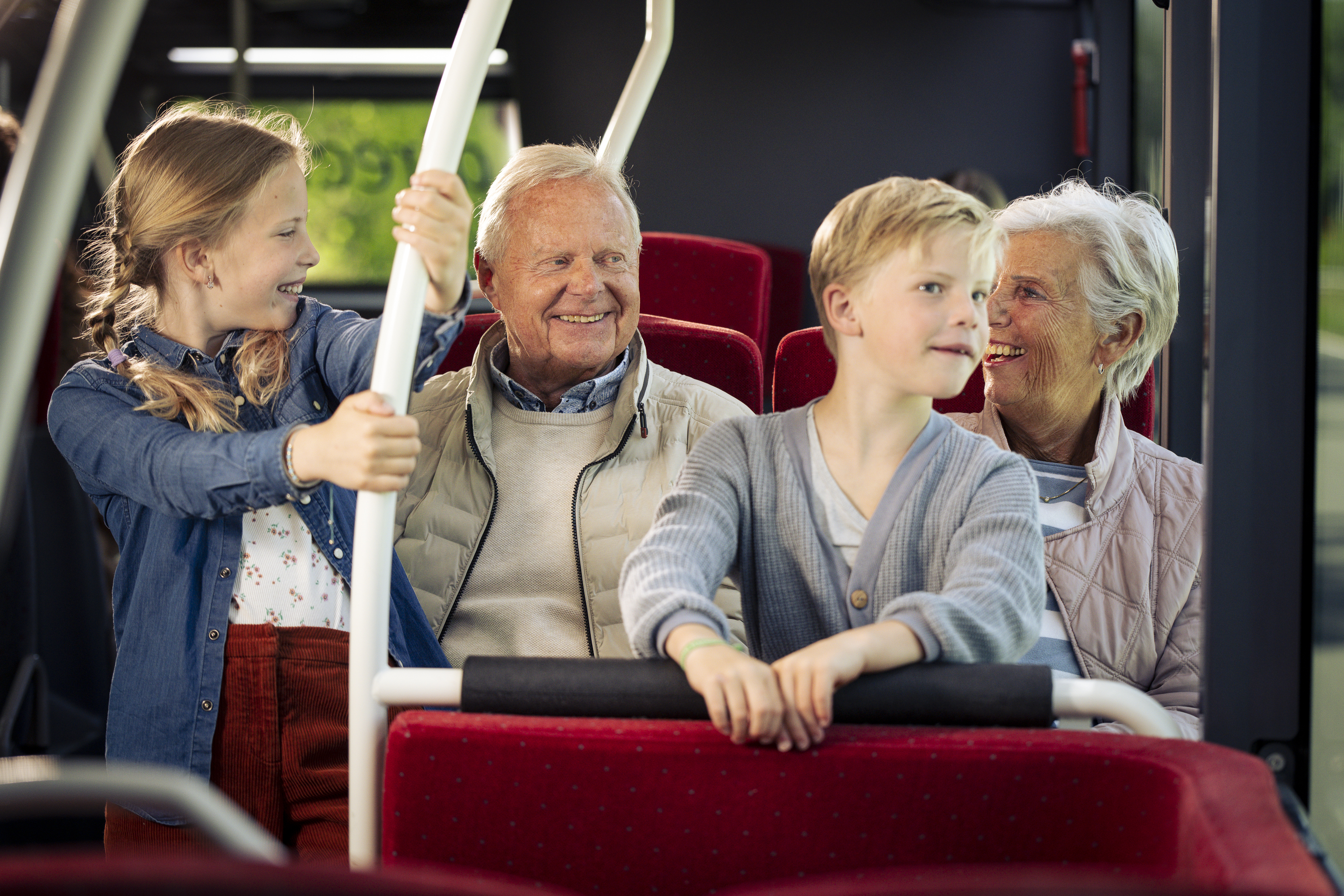 Een opa en oma zitten met hun kleinkinderen in een Arriva-bus. Ze lachen naar elkaar.