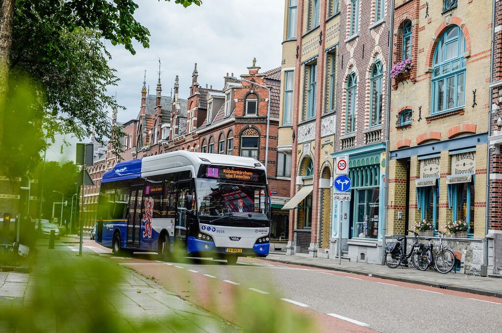 Blauw-witte bus van Arriva rijdt langs kleurige gebouwen in Venlo.
