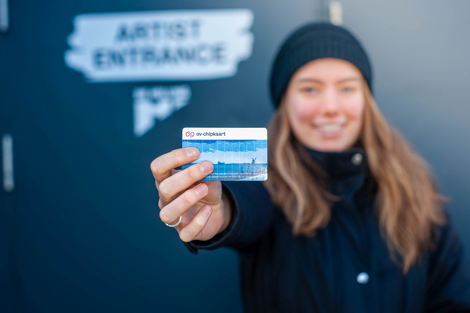 Vrouwelijke reiziger met muts en in winterkleding houdt een blauwe ov-chipkaart richting de camera.