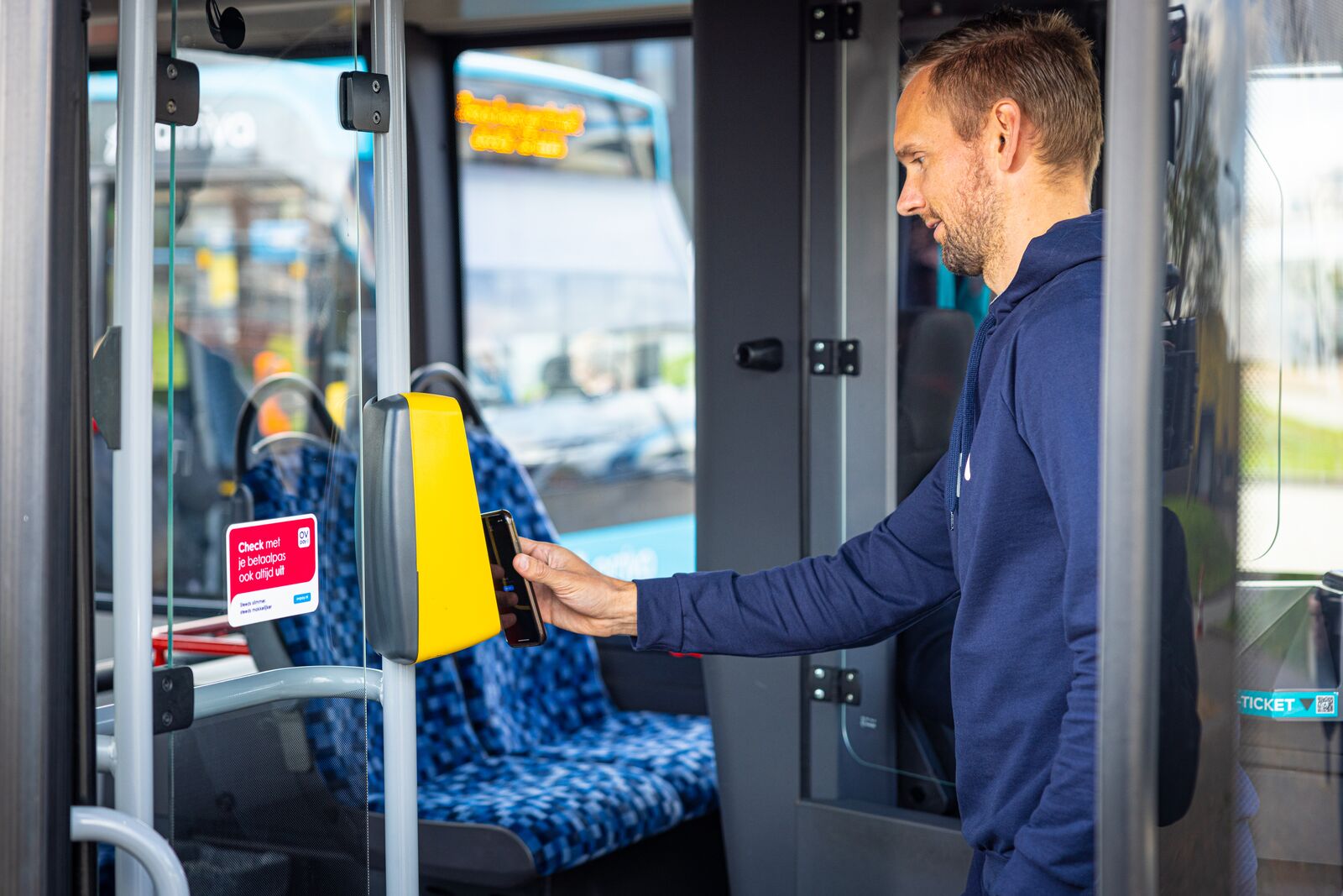 Man checkt met betaalpas op zijn telefoon in bij incheckpaal in bus van Arriva.