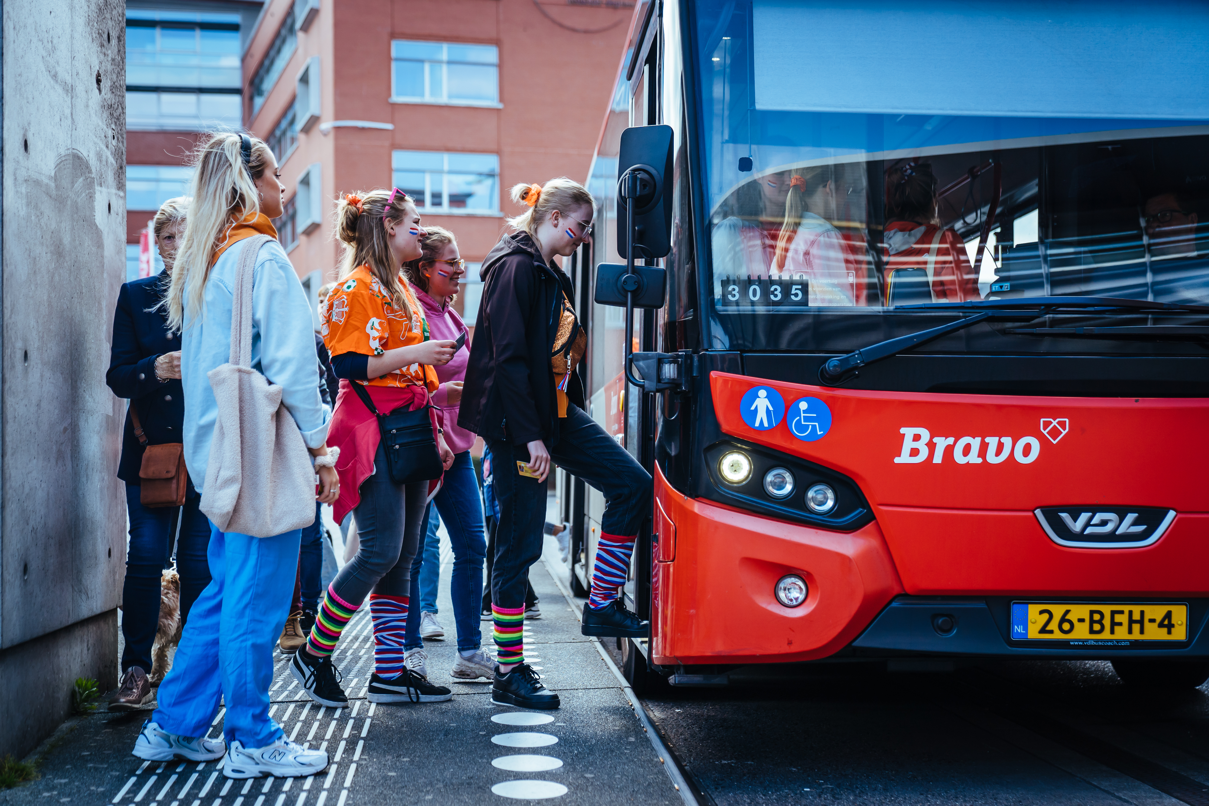 Vrolijk uitgedoste festivalgangers stappen in Bravo-bus tijdens carnaval.